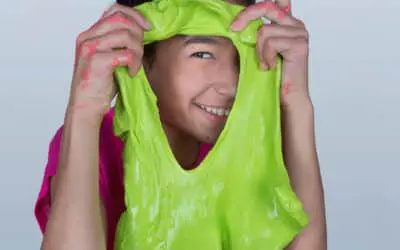 Young girl in pink shirt looks through a hole in green gak