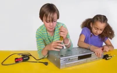 Two middle school girls (one holding a screwdriver) take apart a dvd/vcr machine