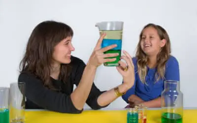 a female engineer presents a glass of layered liquids to a young female student