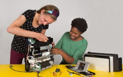 Two women taking apart a printer and smiling