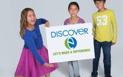 Two students smile while one student dramatically poses with DiscoverE sign