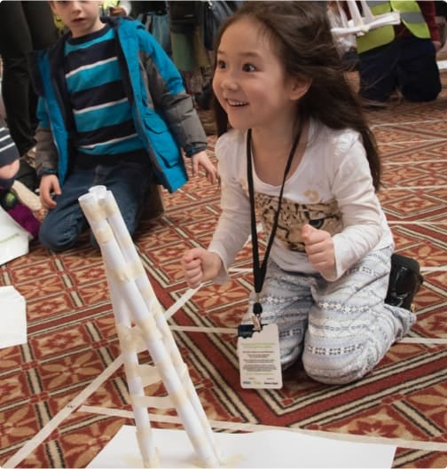 young girl excited about the paper tower she built at an engineering outreach event