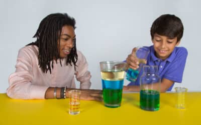 Male engineer excitedly test different colored liquids on a yellow tabletop