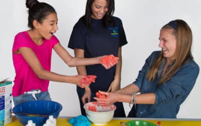 two girls and a female volunteer are playing with gak slime.