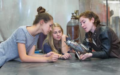 Two girls and a female engineer explore and discuss a small robot