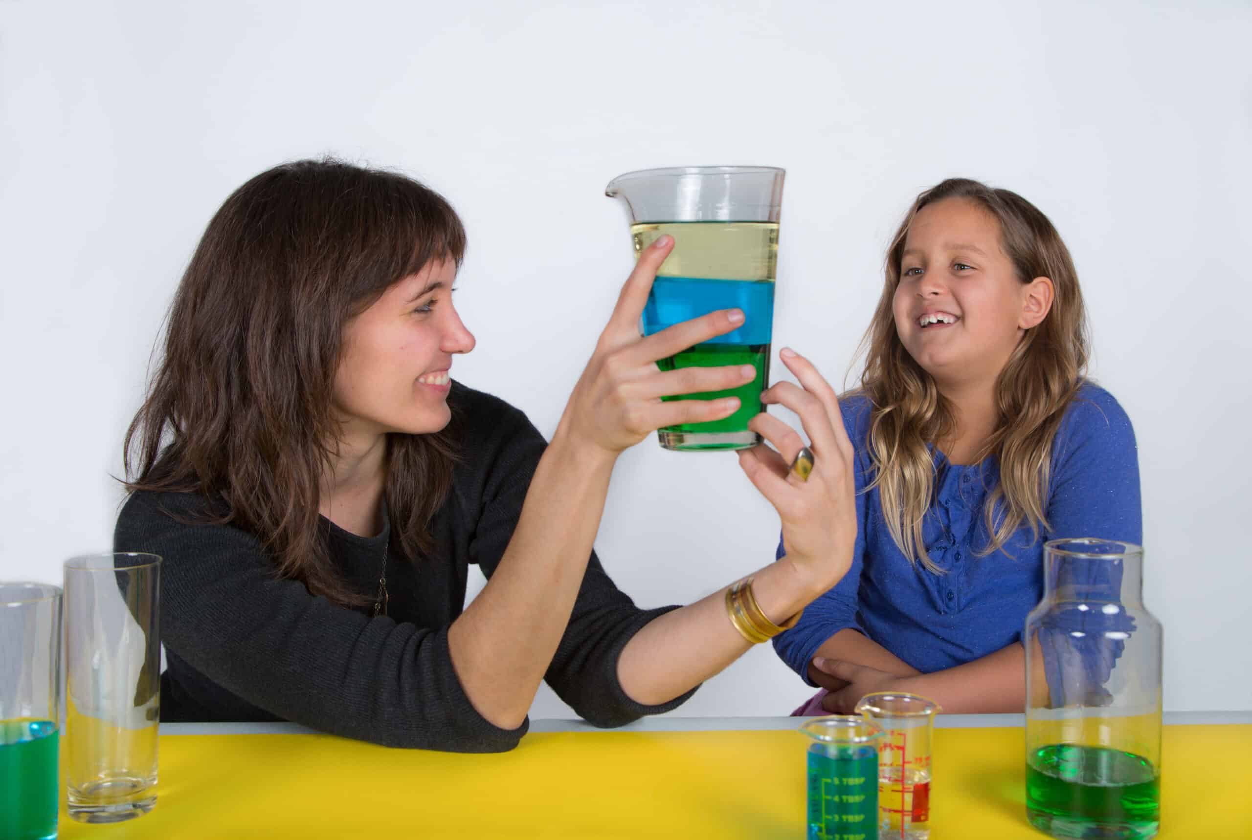 a female engineer presents a glass of layered liquids to a young female student