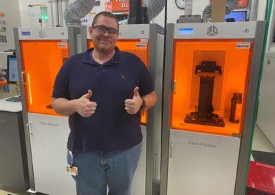 Ben Dopp stands with two thumbs up in front of a 3d printer